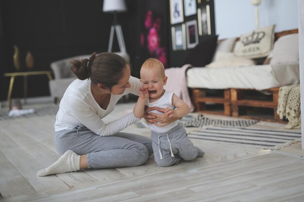 Foto moeder troost een huilende baby op de vloer in een heldere kamer het concept van adoptie van moederschap 10