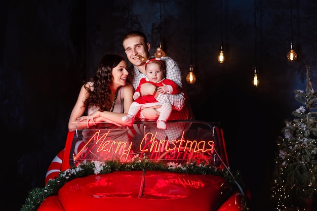 Moeder, vader en babymeisje met plezier in de kerst retro rode auto. Ouders met een dochtertje in een kerstfotosessie.