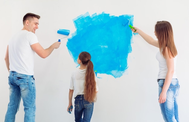 Moeder, vader en dochtertje schilderen de muur in hun nieuwe huis.