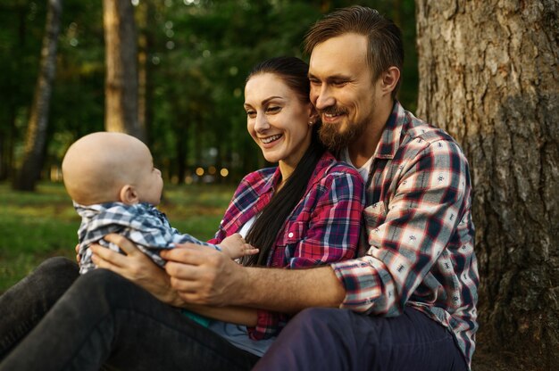 Moeder, vader en kleine baby zitten onder de boom in zomerpark