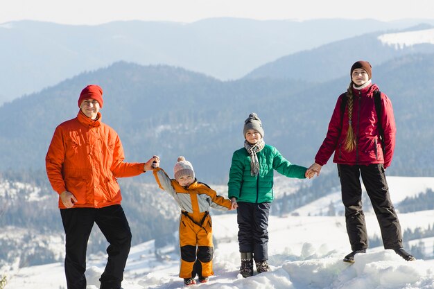 Moeder, vader en twee zonen staan en glimlachen tegen de achtergrond van met sneeuw bedekte bergen. Een blije familie. Winter zonnige dag