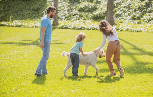 Moeder, vader en zoon rennen met hond in het park, gelukkig jong gezin dat samen buiten tijd doorbrengt