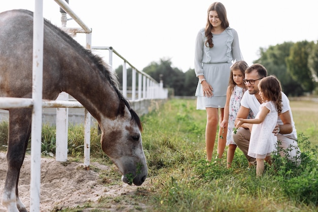 Moeder, vader knuffelen dochters genieten van wandelen op de boerderij en paard kijken. Jong gezin tijd samen doorbrengen op vakantie, buitenshuis.