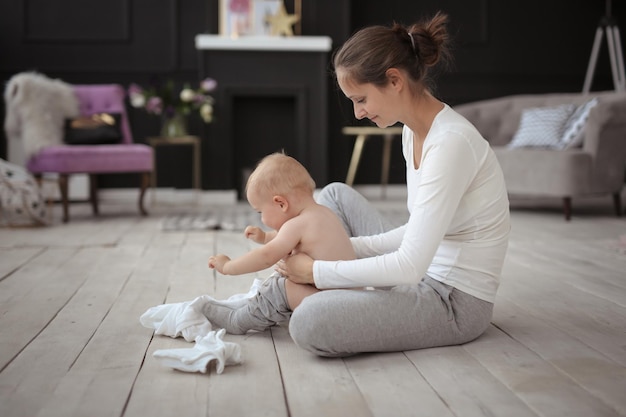 Moeder verandert kleren huilende baby van 10 maanden op de vloer in een gezellig echt licht interieur