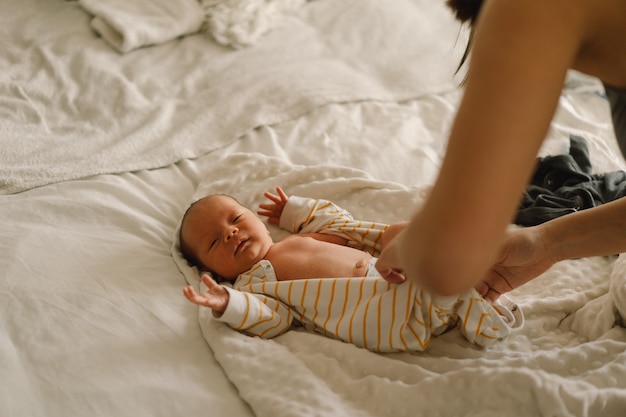 Moeder verandert zijn luier pasgeboren baby. Gelukkig jonge moeder spelen met baby terwijl het veranderen van zijn luier op bed. Gelukkig moederschap