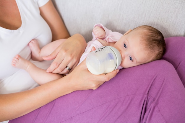 Moeder voedende baby met melkfles in woonkamer