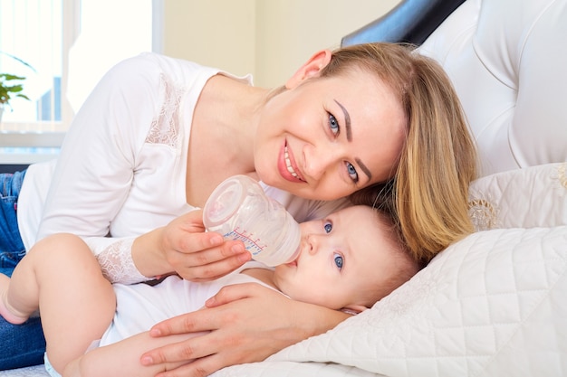 Moeder voedt haar baby uit een fles in bed met eten