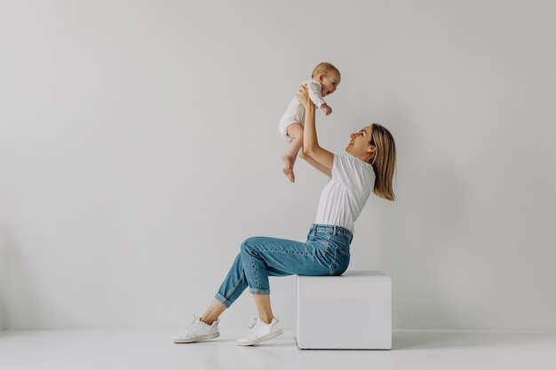 Moeder zit en houdt baby in de lucht glimlachend op witte muur achtergrond