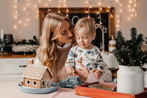 Moeder zit met haar zoon in de keuken aan de tafel met oudjaarsdecor met slingers, houdt hem in haar armen en kijkt hem aan.