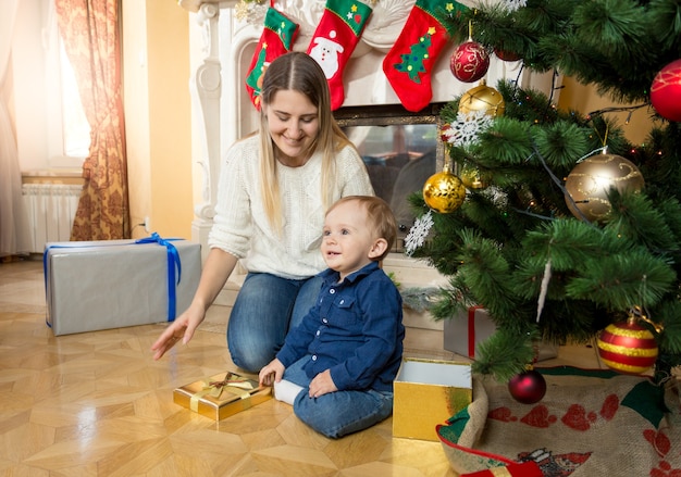 Moeder zit met haar zoontje op de vloer in de woonkamer naast de open haard en de kerstboom