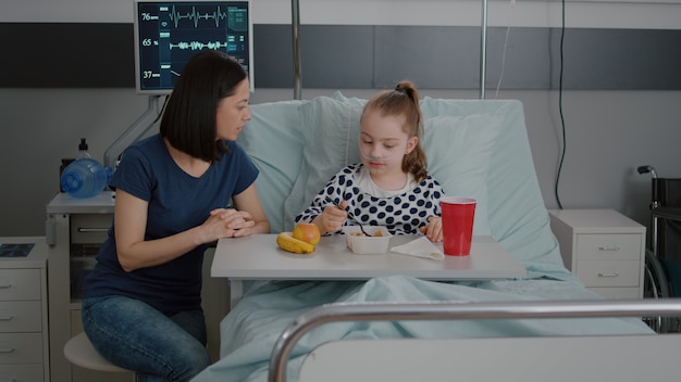 Moeder zit met zieke kindpatiënt terwijl ze gezonde lunch eet op de ziekenhuisafdeling