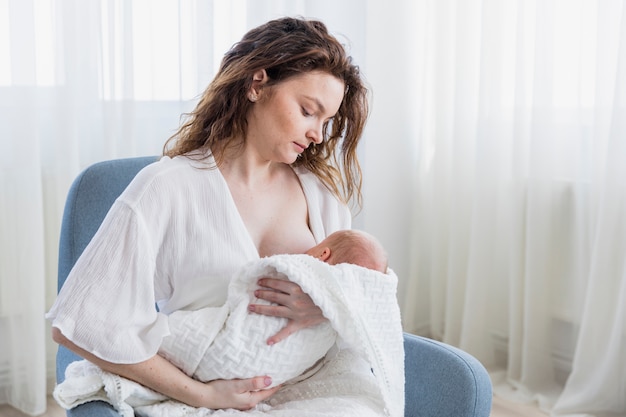 Foto moederborst die haar babyzitting op wapenstoel thuis voeden