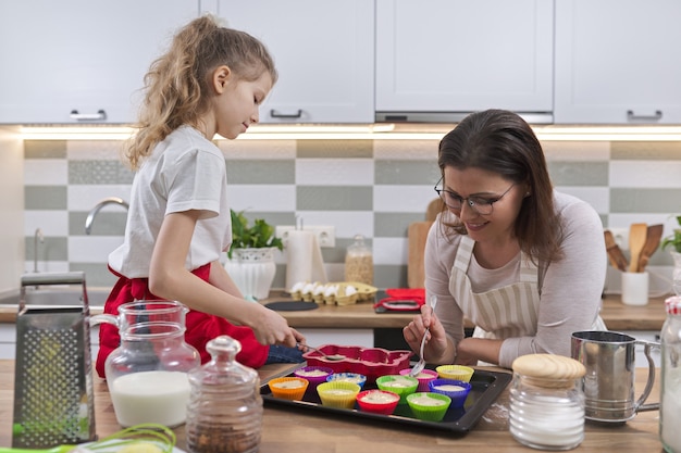 Moederdag, moeder en dochter kind bereiden cupcakes samen thuis in de keuken, vrouw kind koken onderwijs