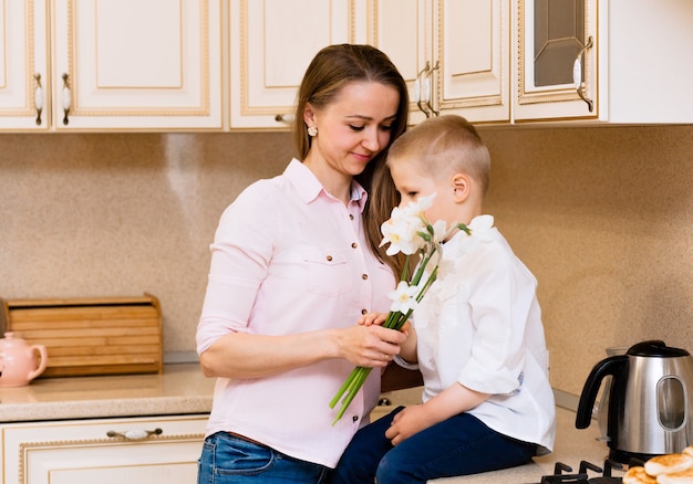 Moederdag, vakantie en familieconcept - gelukkig zoontje geeft thuis bloemen aan zijn lachende moeder. Een kind geeft mama een boeket narcissen