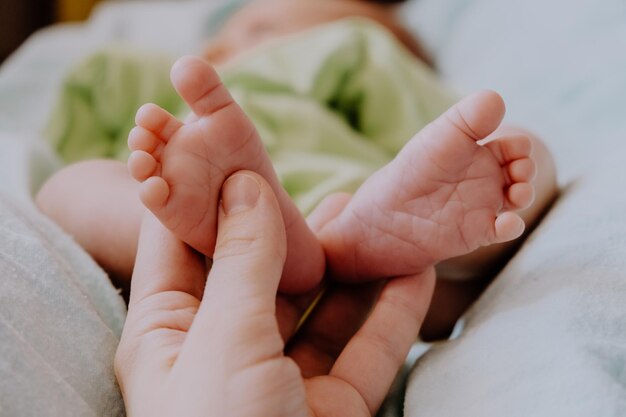 Moederhand die pasgeboren babyvoeten masseert