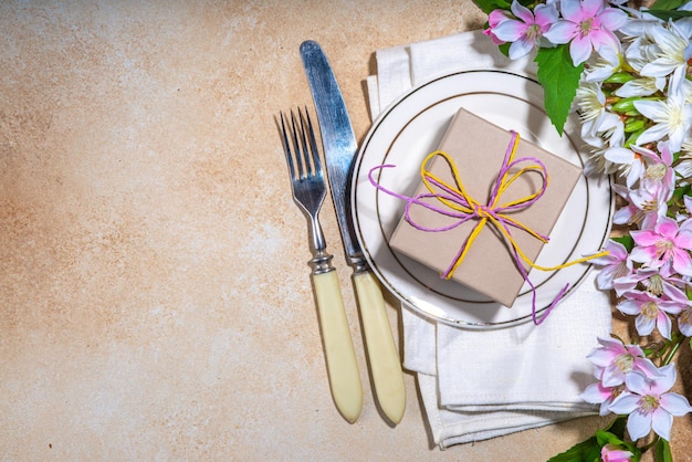 Moeders dag bruiloft verjaardag lente vakantie wenskaart achtergrond Moeders dag tafel instelling flatlay met plaat vork mes lente bloemen geschenkdoos aanwezig met lint bovenaanzicht kopie ruimte