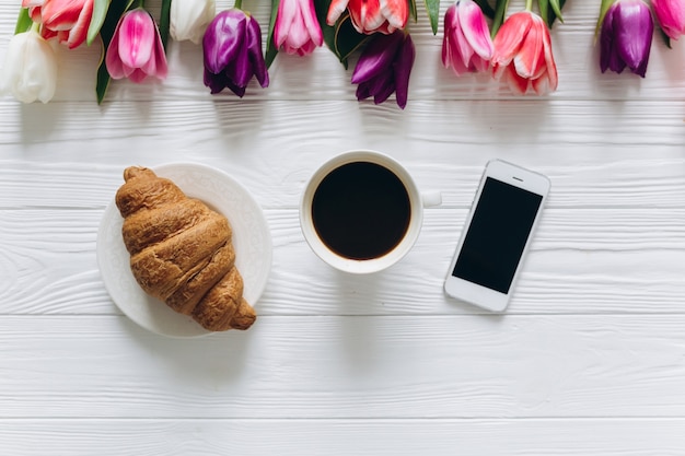 Moeders dag concept. Boeket tulpen, koffie, croissant en smartphone.