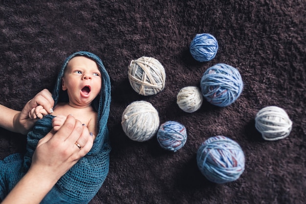 Moeders handen houden de baby vast, gewikkeld in een deken, te midden van wirwar van draad. Prachtig concept van moederliefde. Baby gaapt.