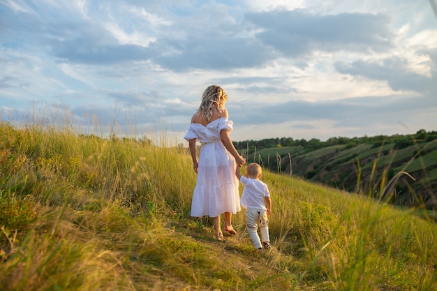 Moederschap. Moeder en baby samen hand in hand. Moeder en zoon lopen bij de hand in het veld. Moederdag. Prachtige natuur met mensen. Loop samen bij de hand