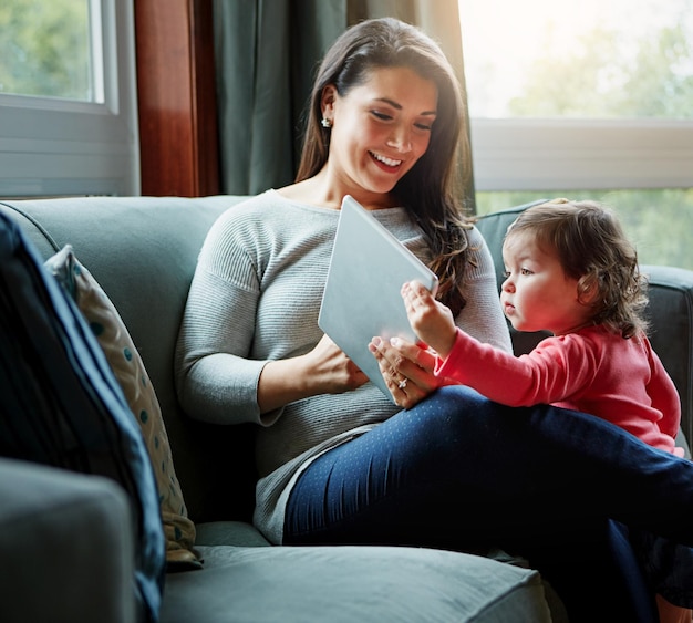 Moedertablet en baby op de bank in de woonkamer voor entertainment, hechting of tijd samen thuis Gelukkige moeder met schattig klein dochtertje of kind ontspannen op de bank met touchscreen in huis