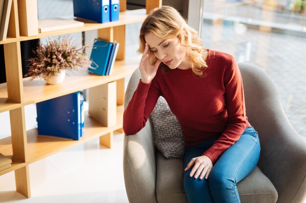 Moeilijke tijden. Ongelukkige aangename jonge vrouw die haar voorhoofd vasthoudt en zich boos voelt tijdens moeilijke tijden in het leven