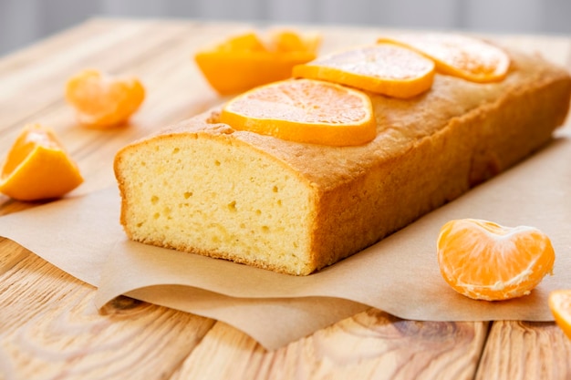 Moist mandarin pound cake on parchment with pieces of fresh tangerine on rustic wooden background Delicious breakfast traditional tea time treat Reciepe of American lemon pie loaf