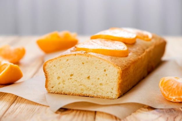 Moist orange fruit pound cake on parchment on rustic wooden background with slices of orange Delicious breakfast traditional English tea time Reciepe of orange pie loaf