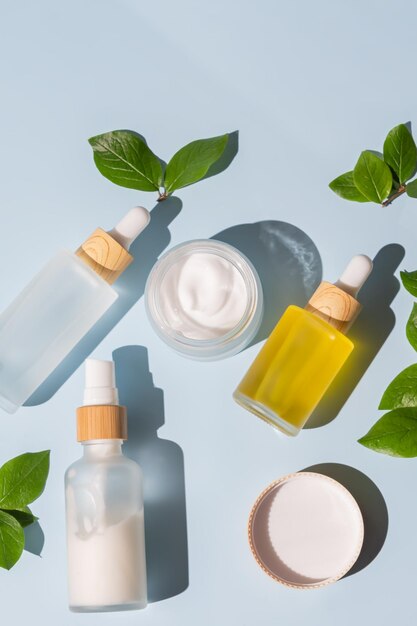 Moisturizer crème pot serum in glazen fles en toner met groene bladeren op blauwe achtergrond Plat lag bovenaanzicht Set voor huid- en lichaamsverzorging schoonheidsproducten Merkloos pakket met blanco etiketten