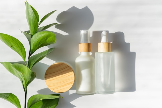 Moisturizer crème pot serum in glazen fles en toner met groene bladeren op witte achtergrond Plat lag bovenaanzicht Set voor huid- en lichaamsverzorging schoonheidsproducten Merkloos pakket met blanco etiketten