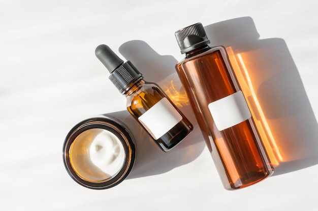 Moisturizer crème pot serum in glazen fles en toner met groene bladeren op witte achtergrond Plat lag bovenaanzicht Set voor huid- en lichaamsverzorging schoonheidsproducten Merkloos pakket met blanco etiketten