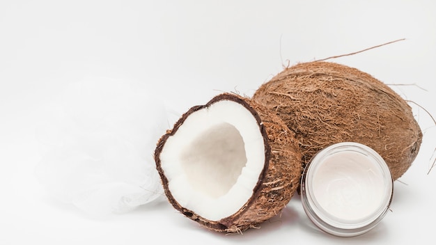 Moisturizing cream; loofah and coconut on white surface