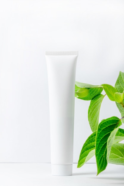 Moisturizing face and eyelid cream with natural extracts. White cosmetic tube with fresh herbs