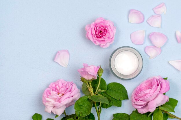 Moisturizing white cream in plastic jar and pink roses top view\
organic cosmetics body creme with natural ingredientspink damask\
rose budscopy spacetop view