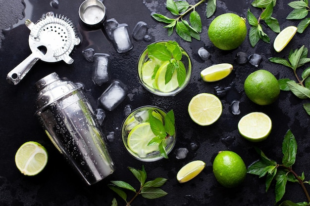 Mojito cocktail alcohol bar longdrink maken munt limoen rum ijs ingrediënten sap soda water shaker en bar gebruiksvoorwerpen op zwarte stenen achtergrond bovenaanzicht plat lag