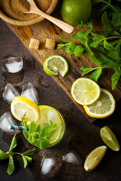 Mojito cocktail ingredients, fresh mint, lime, lemon, sugar, ice on a dark. 