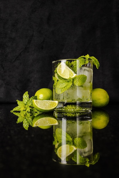 Mojito cocktail and lime and mint aside on black reflected surface and black background