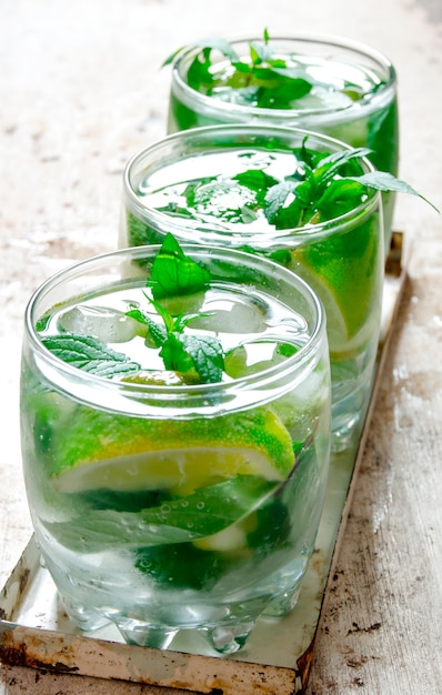 Mojito cocktail. Three cocktail glasses with ice cubes, lime, mint leaves and rum on rustic table