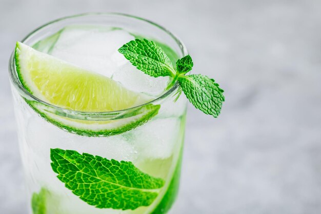 Mojito cocktail with ice fresh mint and lime in glass on gray stone background Refreshing ice cold summer drink