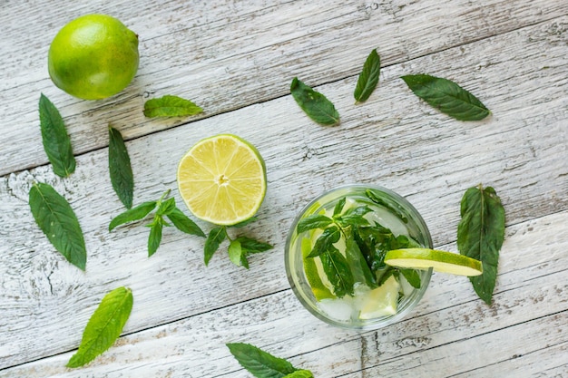 Mojito cocktail con lime e menta nel bicchiere highball su un tavolo di legno bianco