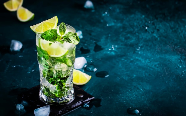 Cocktail mojito con rum bianco lime, soda, zucchero di canna, menta e ghiaccio in vetro su sfondo blu intenso spazio negativo