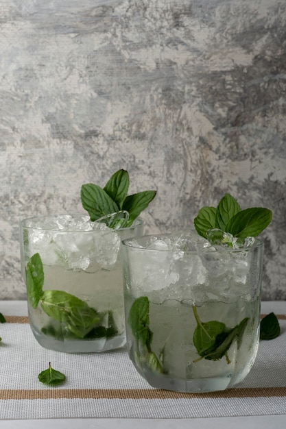 Mojito geserveerd in een kristalglas met schijfjes citroen en muntblaadjes op een witte tafel