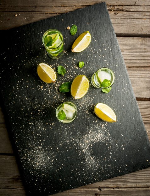 Mojito or lemonade with pieces of lemon lime mint leaves on a black concrete background with ice c