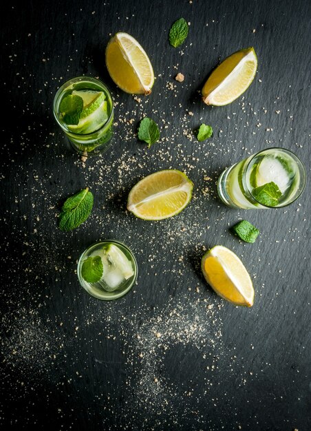 Mojito or lemonade with pieces of lemon lime mint leaves on a black concrete background with ice c