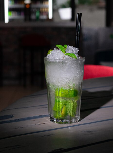 Mojito Long Drink gedecoreerd met limoen en munt met crushed ijs. In een glazen beker collins. Op een grijze houten achtergrond. Detailopname. Hard licht