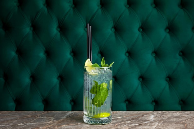 Mojito rum alcoholische cocktail geserveerd in een longdrinkglas met ijsblokjes gegarneerd met citroen en munt aan de bar