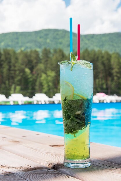 Mojitococktail met limoen en munt in longdrinkglas bij het zwembad op de zomerbergachtergrond