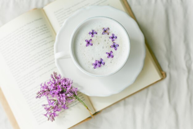 Mok cappuccino op een beige ondergrond. Lila bloemen, boek.