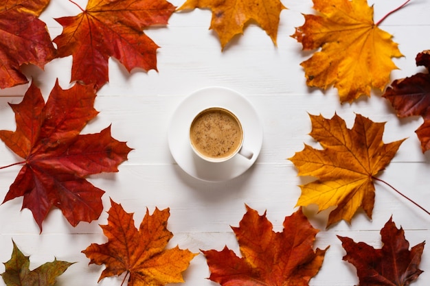 Mok koffie met melk op witte houten tafel in compositie met herfst esdoorn bladeren