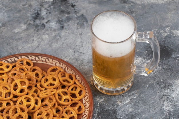 Mok koud schuimend bier en gezouten pretzels op marmeren oppervlak