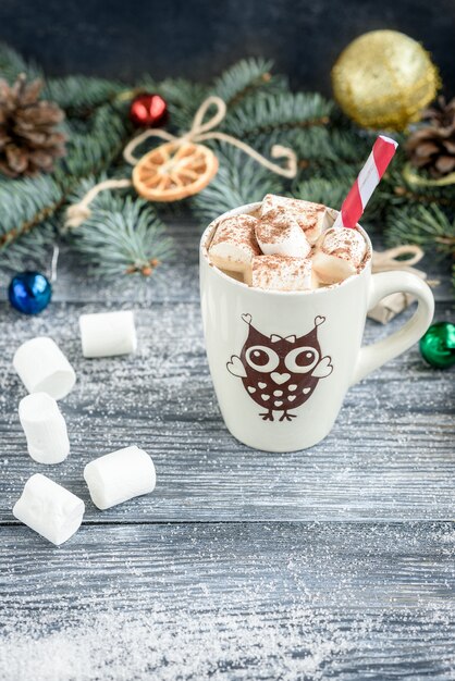 Mok met warme chocolademelk en marshmallow op Kerstmis achtergrond met fir takken, kegels en ballen op grijze houten tafel.